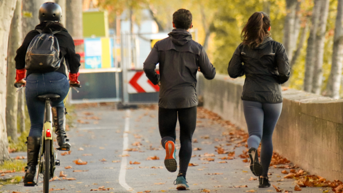 Cyclist riding on a bike lane parallel to 2 joggers facing forward.