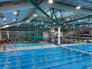 Wide shot inside of Saanich Commonwealth Placem showing a large lane pool, with a waterslide and more pool in the distance. 