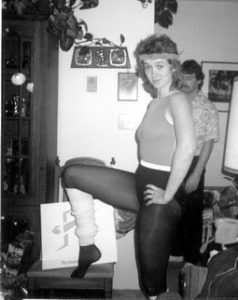 A black and white photo of young Christina Truscott, circa 1986. Christina is posing with one leg up, wearing a leotard, tights, and legwarmers. 